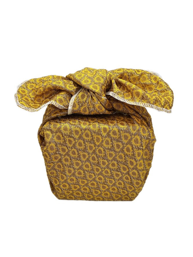 Gift wrapped in yellow and gold embossed polyester fabric with a textured sunburst pattern, full tied folds and white overlocked edging