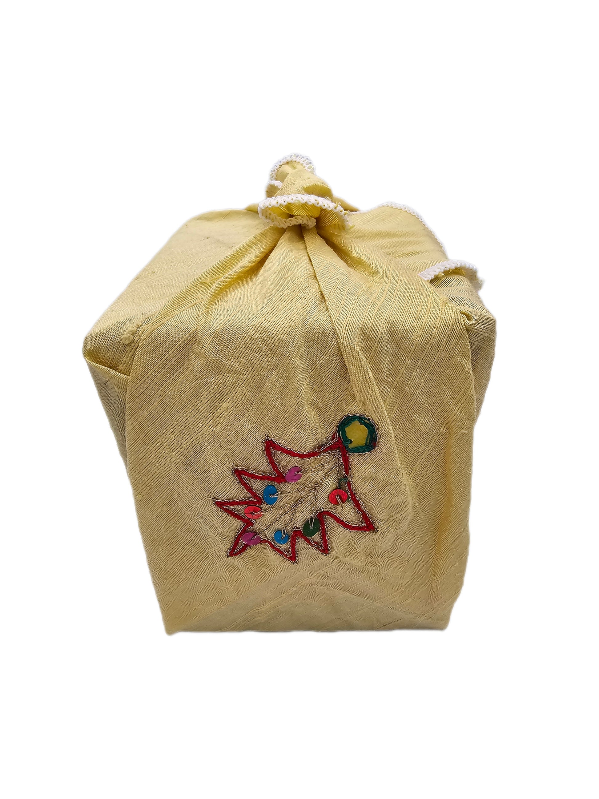 Square gift wrapped in golden raw silk with embroidered Christmas-tree motifs, multicoloured sequins and white overlocked edging, tied at the top