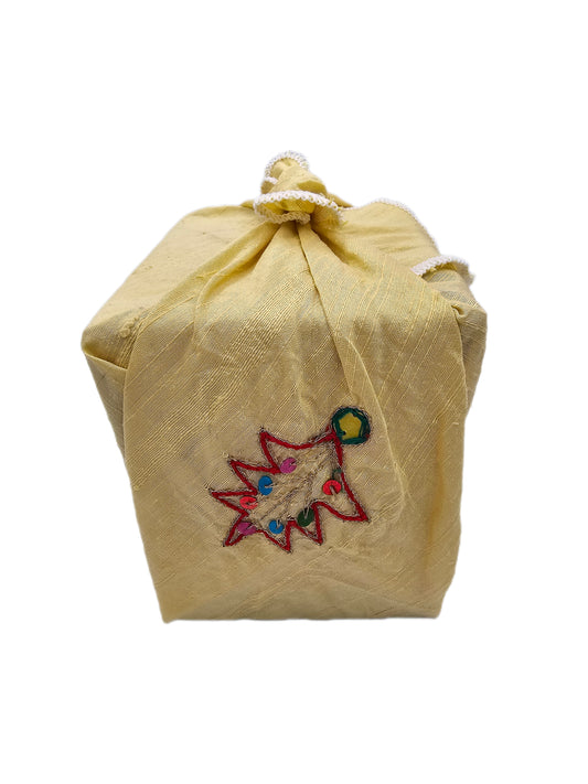 Square gift wrapped in golden raw silk with embroidered Christmas-tree motifs, multicoloured sequins and white overlocked edging, tied at the top