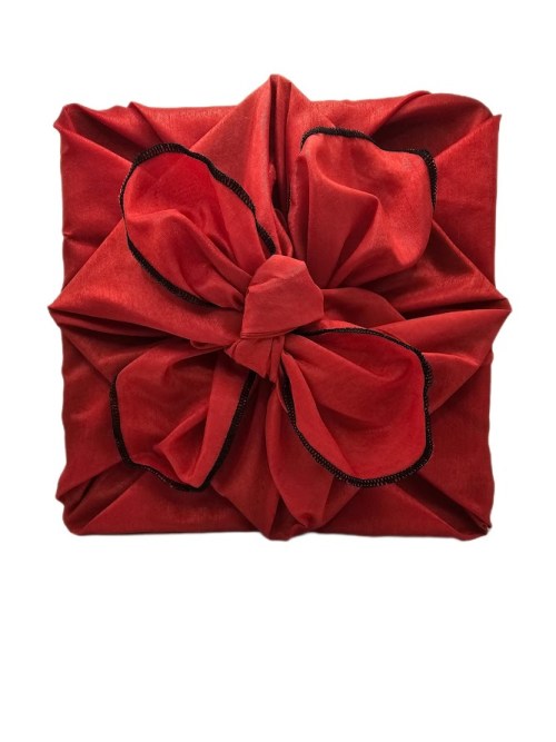 Square gift wrapped in vivid red polyester fabric with a structured decorative knot and contrasting black overlocked edging