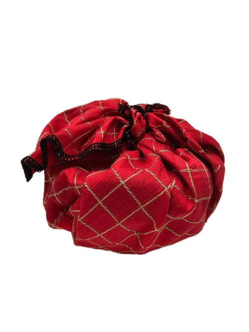 Round gift wrapped in red raw silk with raised gold-coloured lattice embroidery and contrasting black overlocked edging, tied in a structured knot