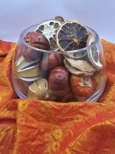 Glass bowl of decorative dried fruit resting on orange patterned silk fabric before wrapping