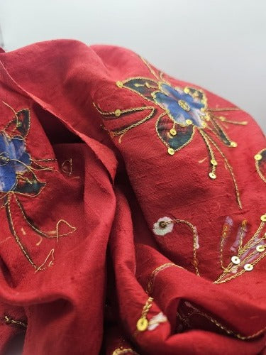 Close-up of deep red raw silk showing its textured grain, printed flowers, firm gold-coloured thread detail and gold sequins