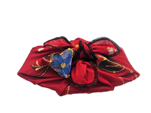 Rectangular dish wrapped in deep red raw silk with floral and gold sequin detailing, tied at the top with structured loops and black edging
