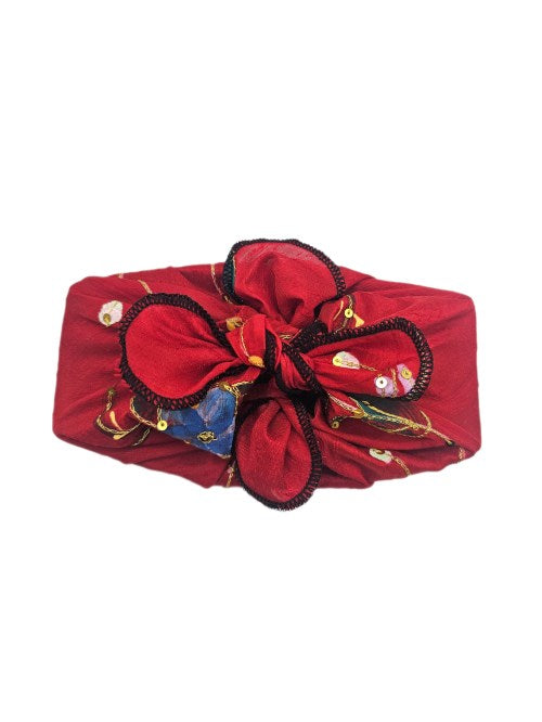 Gift wrapped in deep red raw silk with printed floral detail, gold-coloured sequins and black overlocked edging, tied in a structured sculpted knot
