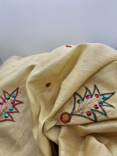 Close-up of golden raw silk showing its textured grain, raised red, green and gold embroidery and multicoloured sequins