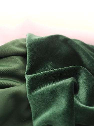 Close-up of deep green velour fabric showing the soft plush pile, smooth reverse and black overlocked edge