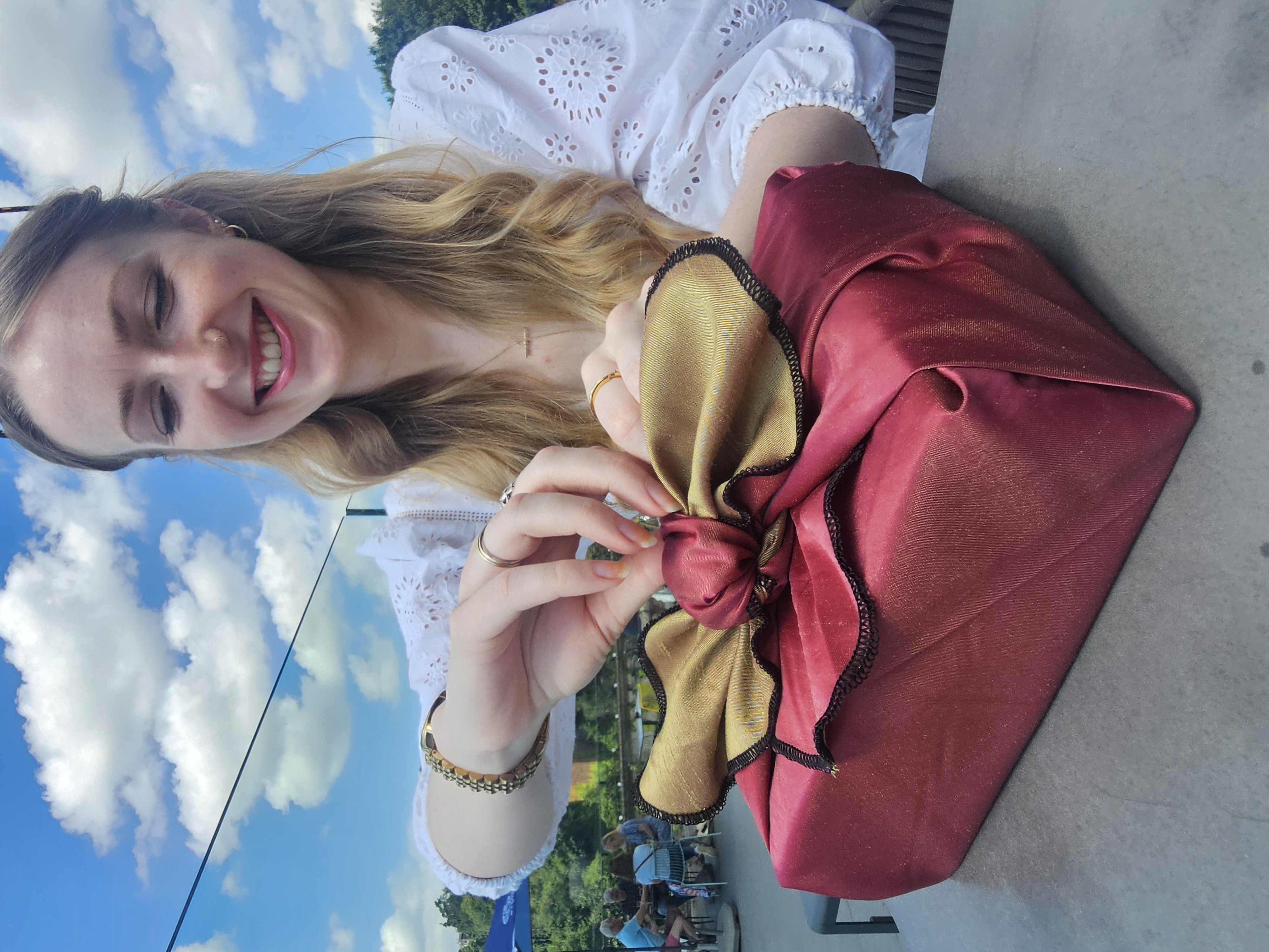 Young lady with strawberry blonde hair starting to undo the knot of a two tone, burgundy and green fabric wrapped gift