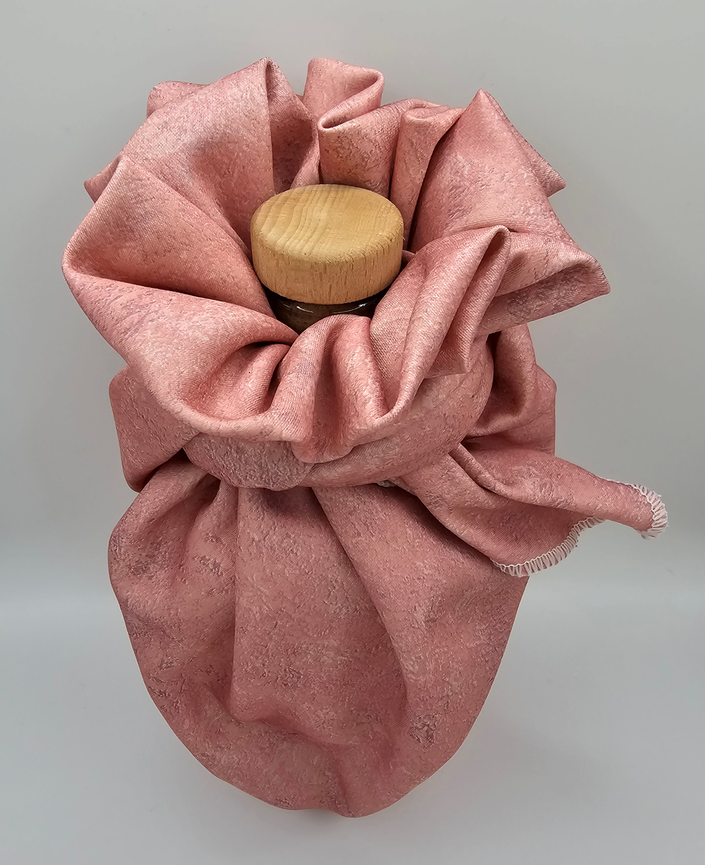 Image of a fabric gift wrapped bottle in the style of a flower, with the light wooden bottle stopper visible