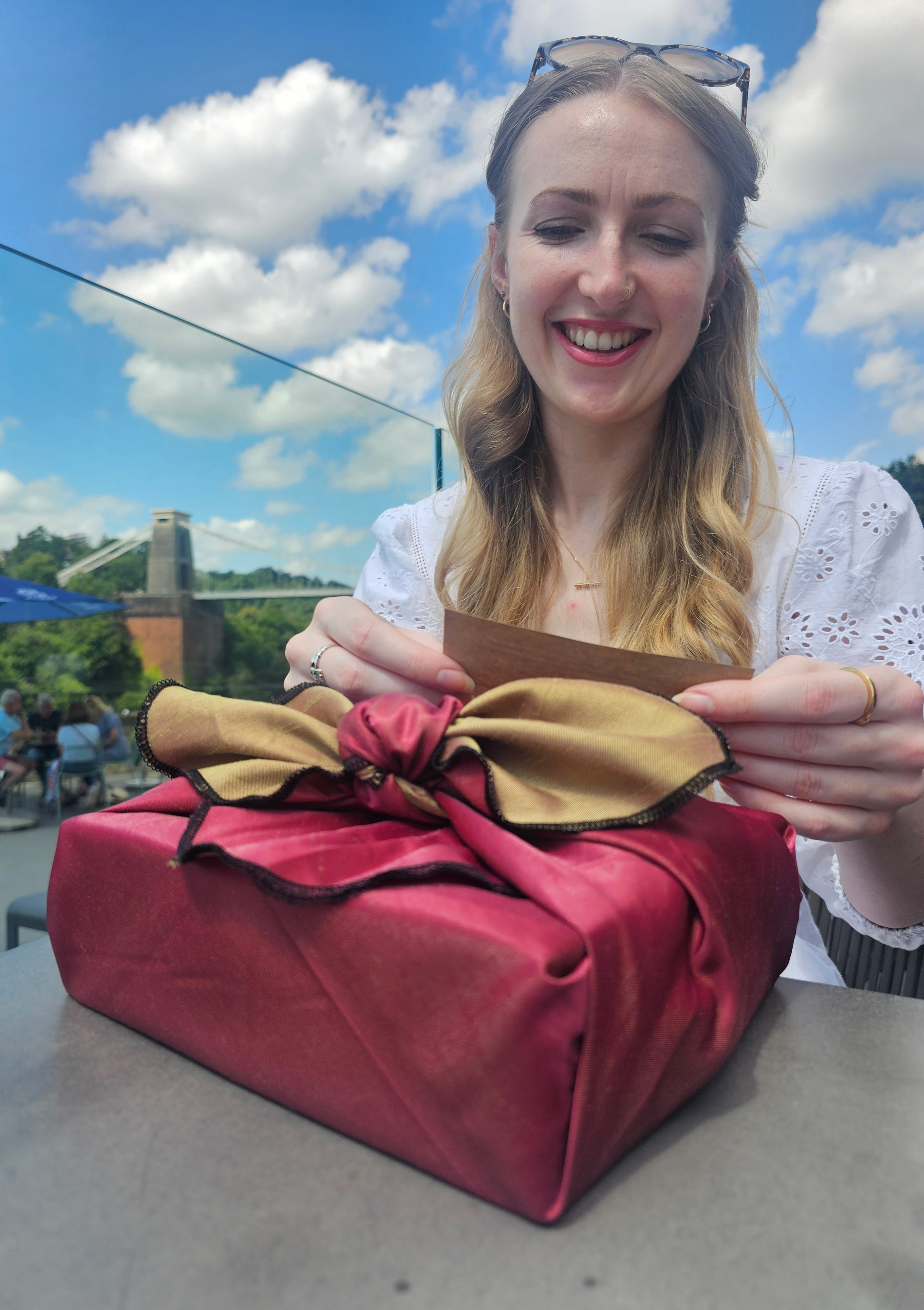 Image of a young lady with strawberry blonde hair reading a gift tag from a fabric wrapped gift