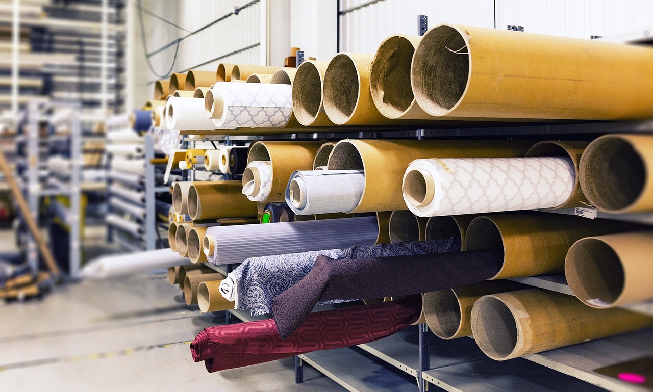 Image with many cardboard rolls on shelves, some with fabric around them, some plain cardboard rolls and some with fabric around them in larger protective tubes