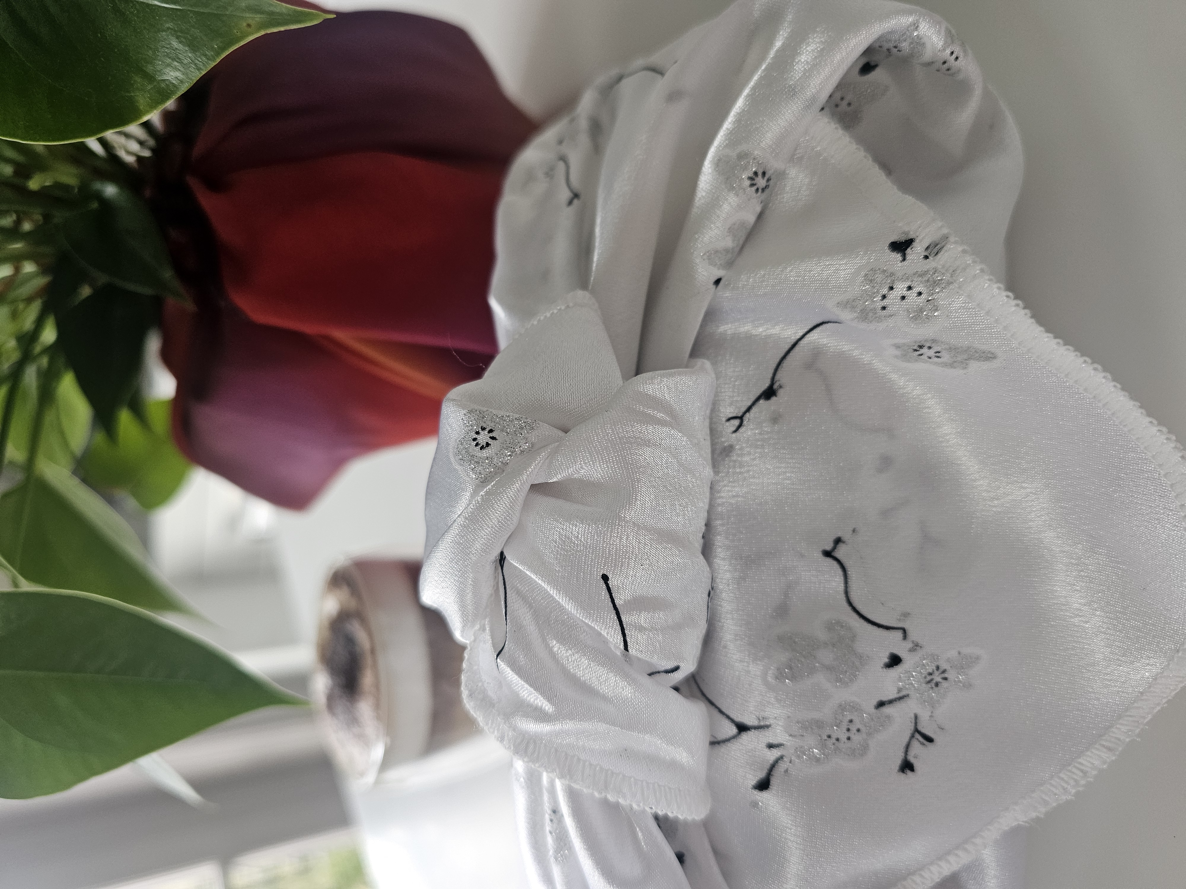 white fabric wrapped gift with plant behind with pot wrapped with red fabric wrap